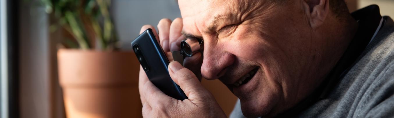 Mies katsoo kännykän ruutua pienellä suurentavalla luupilla.